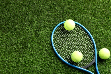 Photo of Tennis racket and balls on green grass, flat lay. Space for text