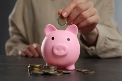 Woman putting coin into pink piggy bank at black table, closeup