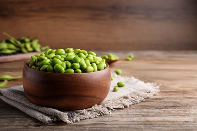 Photo of Bowl of delicious edamame beans on wooden table, space for text