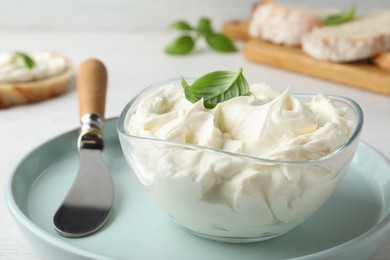 Tasty cream cheese with basil and knife on white wooden table