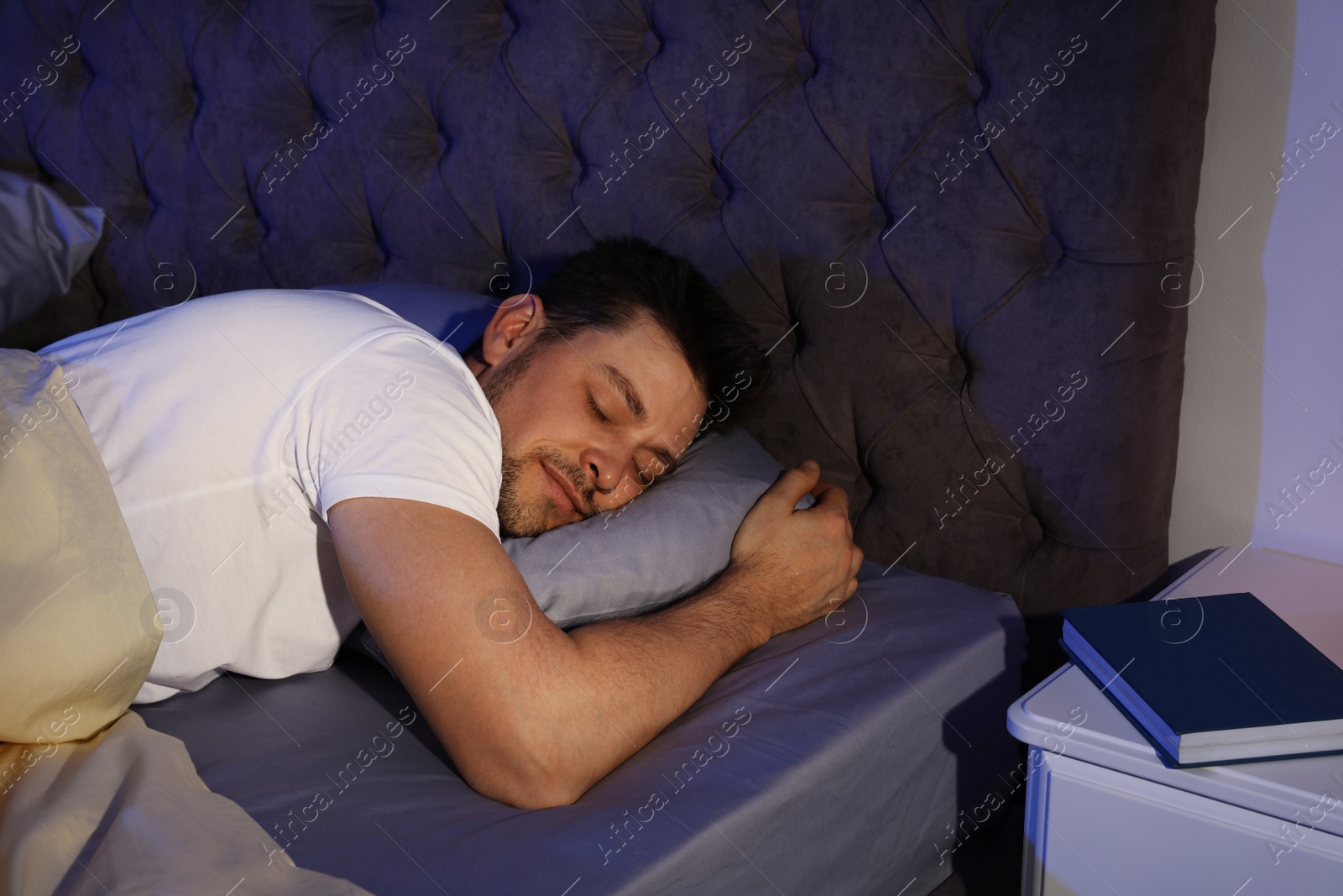 Photo of Handsome man sleeping on pillow in dark room at night. Bedtime