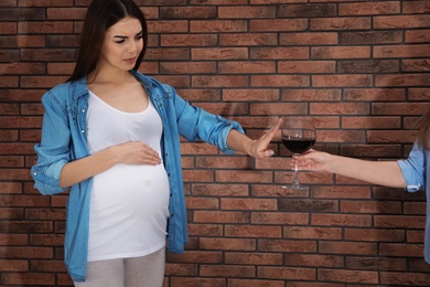 Future mother refusing glass of wine against brick wall. Alcohol abuse during pregnancy