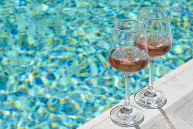 Glasses of tasty rose wine on swimming pool edge, space for text