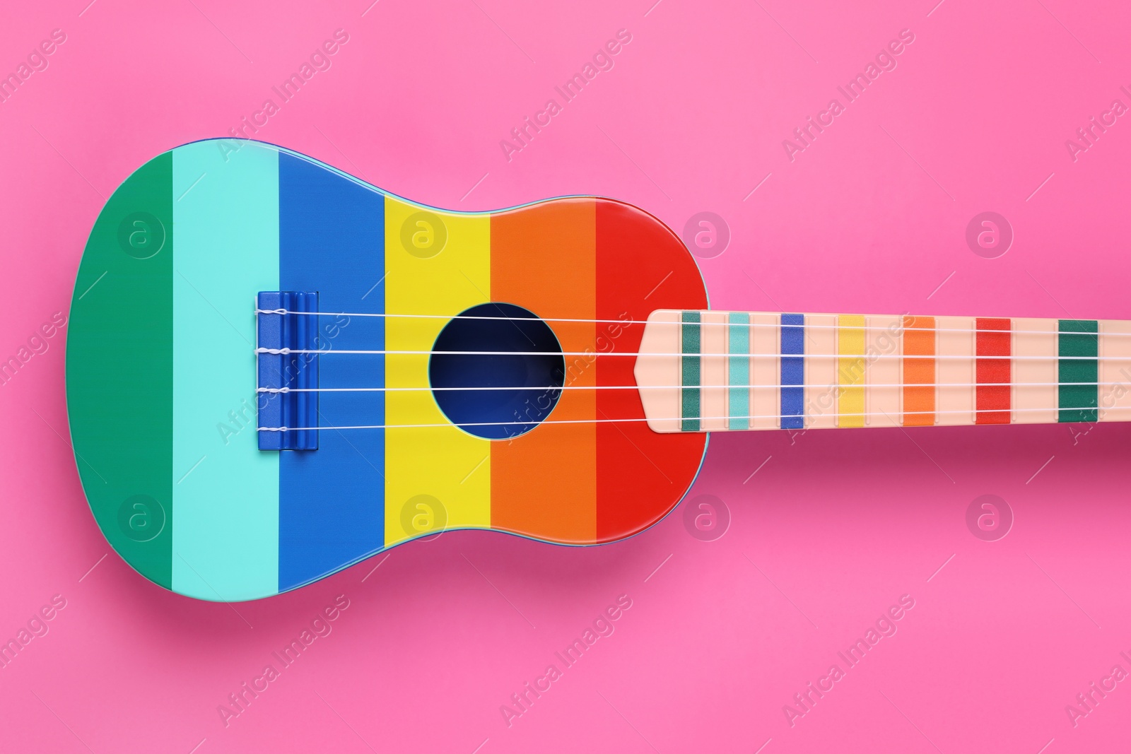 Photo of Colorful ukulele on pink background, top view. String musical instrument