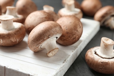 Photo of Fresh champignon mushrooms on wooden cutting board, closeup