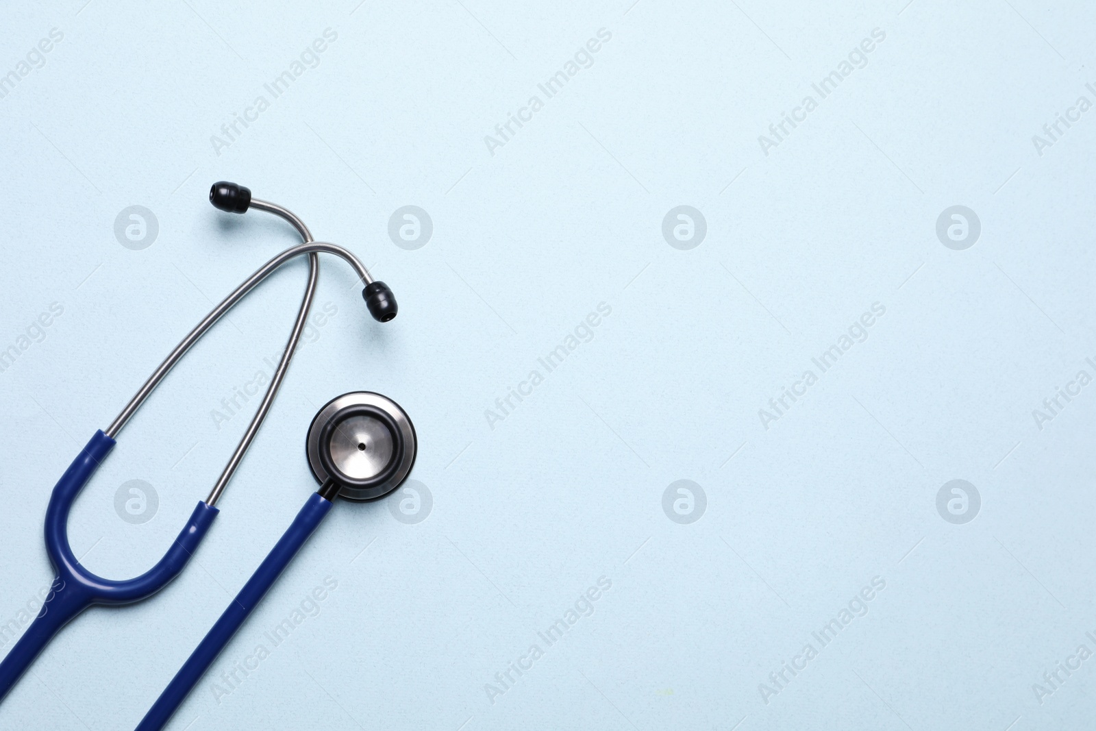 Photo of Stethoscope on light blue background, top view. Space for text