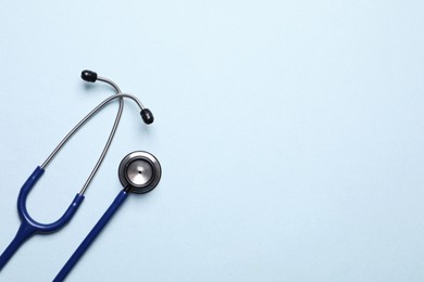 Stethoscope on light blue background, top view. Space for text