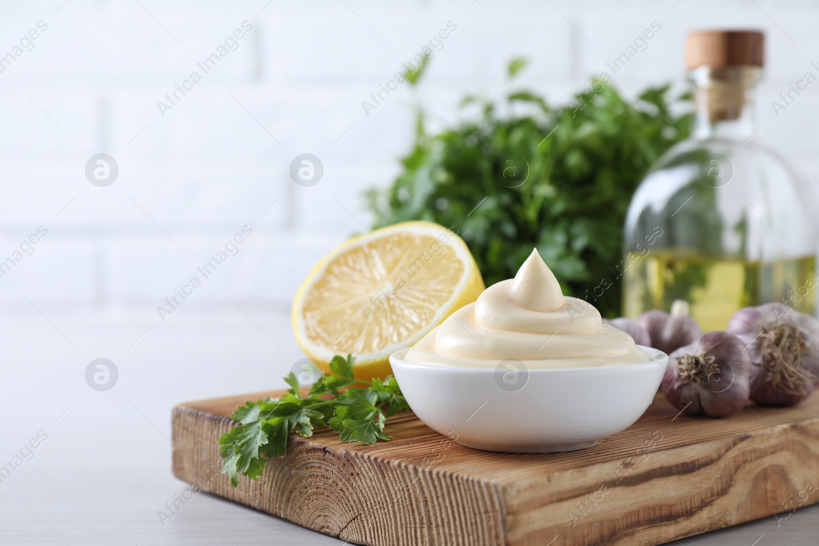 Photo of Tasty mayonnaise sauce in bowl, parsley, garlic and lemon on white wooden table, closeup. Space for text