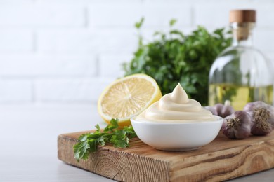 Tasty mayonnaise sauce in bowl, parsley, garlic and lemon on white wooden table, closeup. Space for text