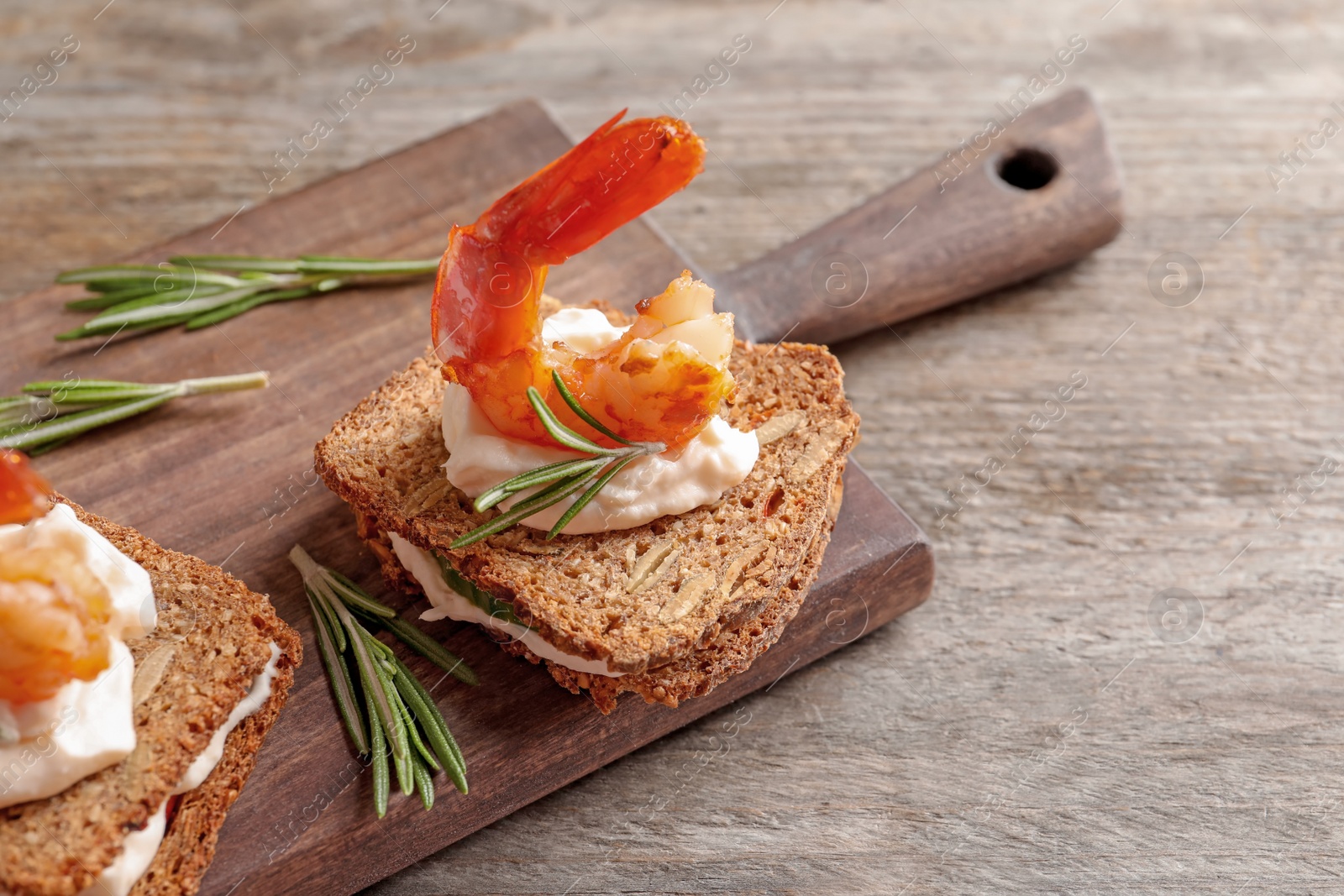 Photo of Delicious small sandwiches with shrimps on wooden board