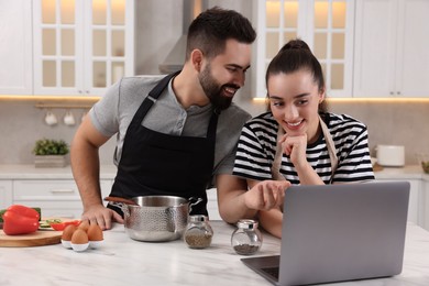 Happy lovely couple using laptop while cooking in kitchen