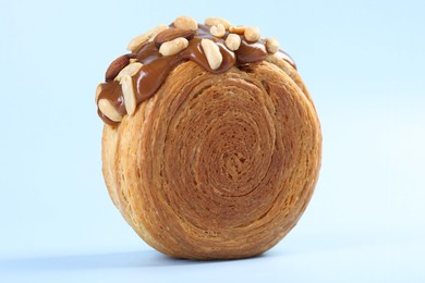 One supreme croissant with chocolate paste and nuts on light blue background, closeup. Tasty puff pastry