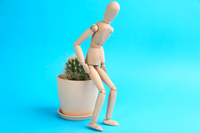 Photo of Wooden human figure and cactus on light blue background. Hemorrhoid problems
