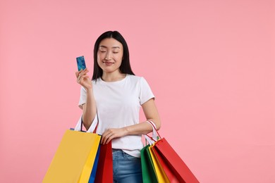Photo of Beautiful woman with shopping bags and credit card on pink background. Space for text