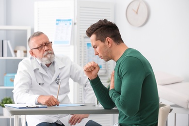 Coughing young man visiting doctor at clinic