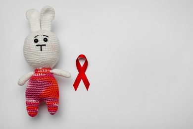 Photo of Cute knitted toy bunny and red ribbon on light grey background, flat lay with space for text. AIDS disease awareness