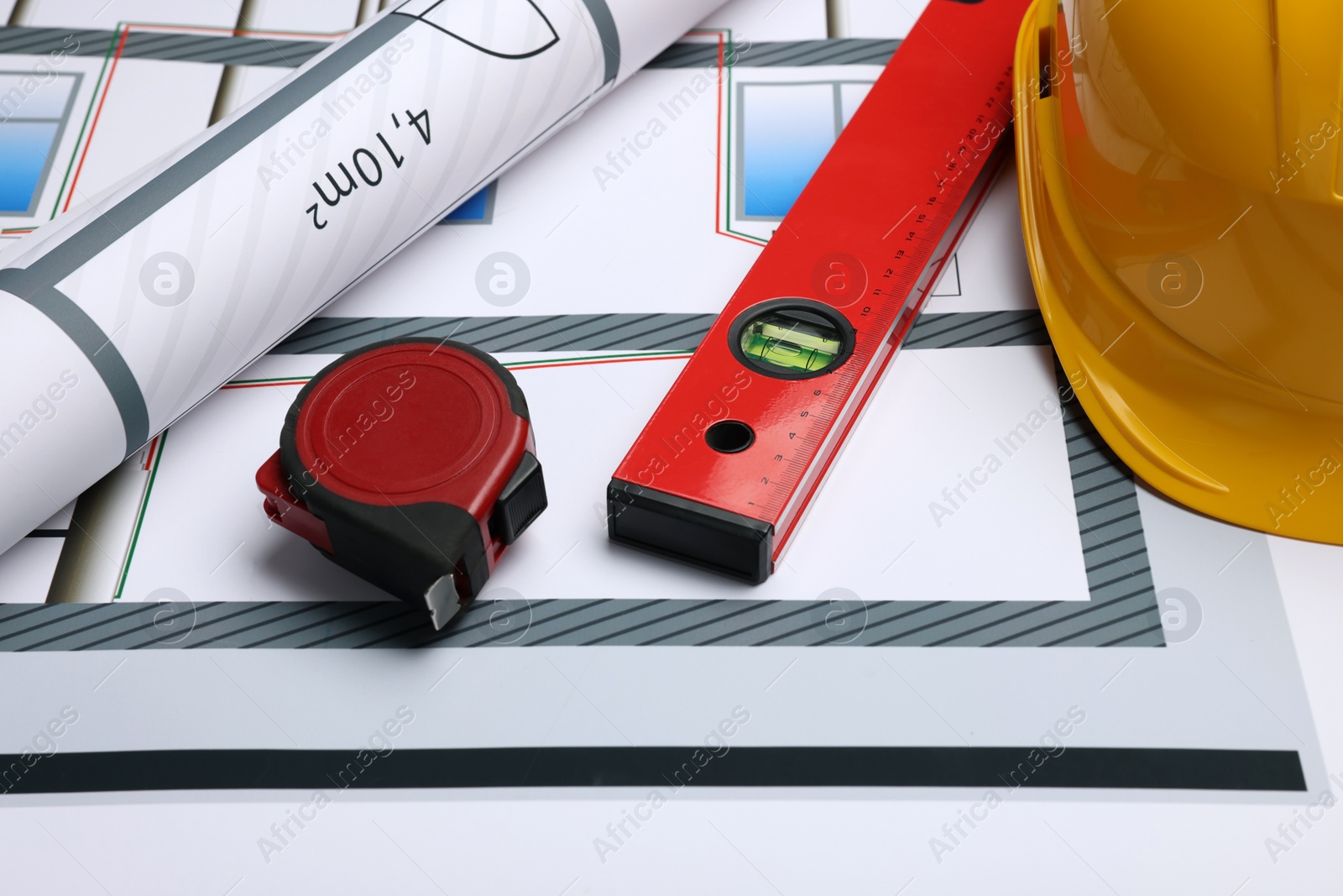 Photo of Construction drawing, safety hat, tape measure and bubble level on house plan, closeup