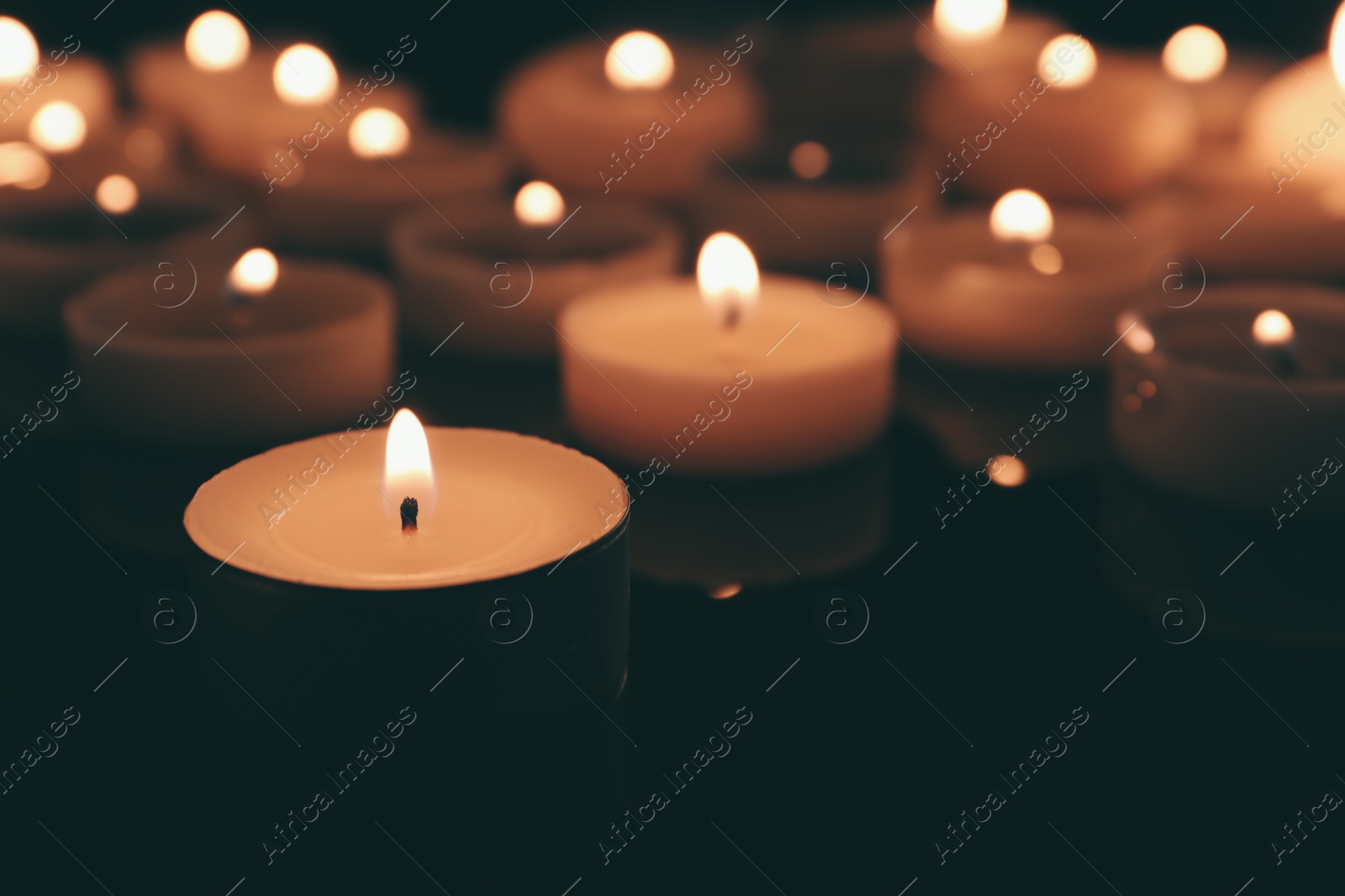 Photo of Wax candles burning on table in darkness, closeup