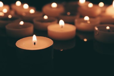 Photo of Wax candles burning on table in darkness, closeup