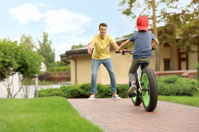 Photo of Dad teaching son to ride bicycle outdoors