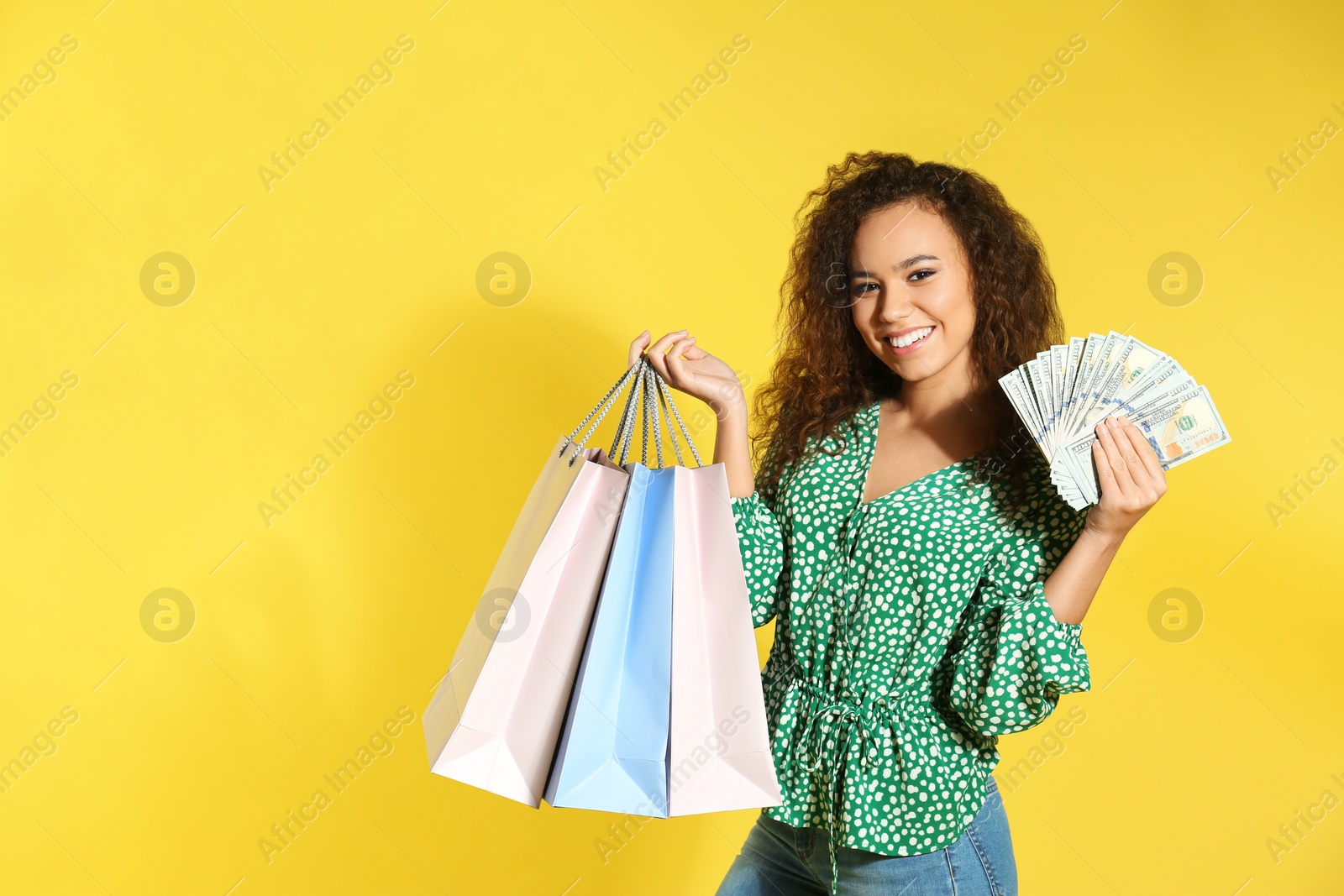 Photo of Young African-American woman with money and shopping bags on color background. Space for text