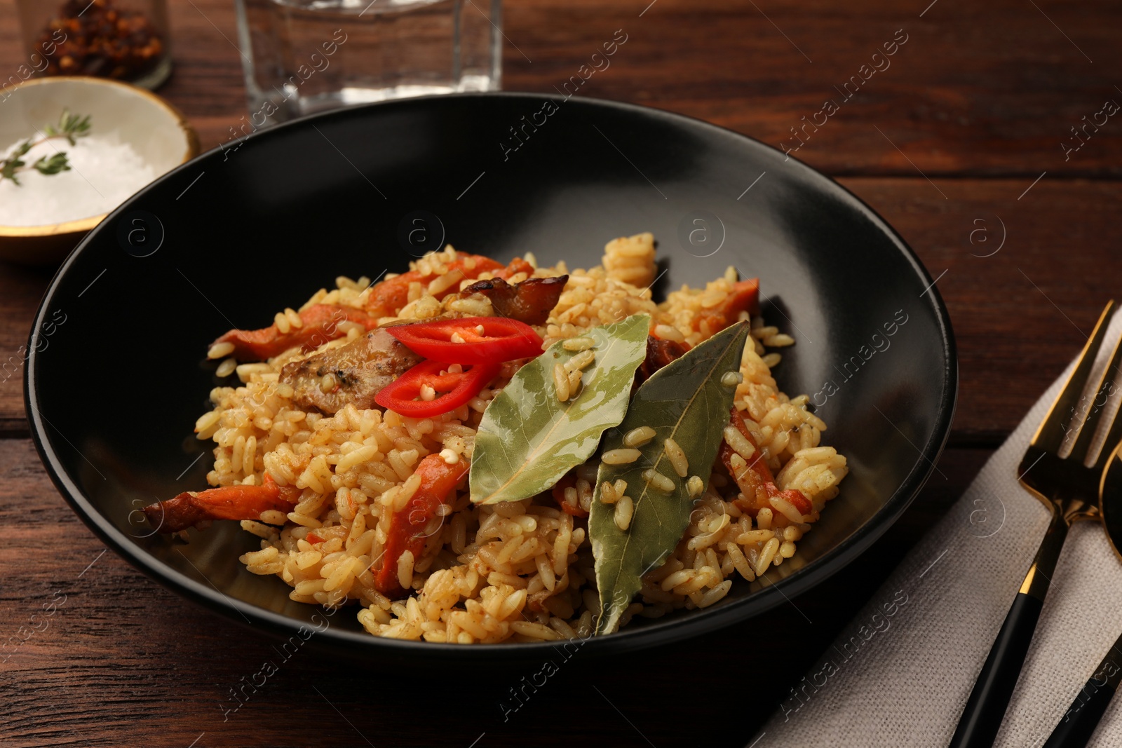Photo of Delicious pilaf and bay leaves in bowl on wooden table