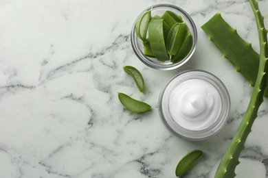 Jar with cream and cut aloe leaves on white marble table, flat lay. Space for text