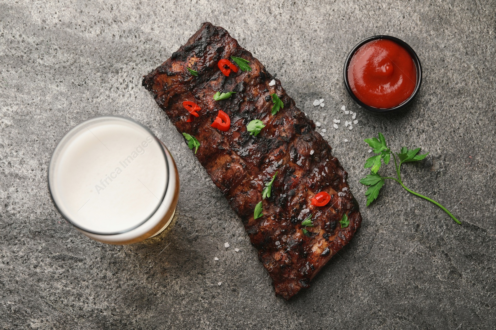 Photo of Glass of beer, tasty grilled ribs and sauce on grey table, flat lay