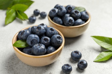 Photo of Tasty fresh blueberries in bowls on light grey table, closeup