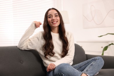 Photo of Beautiful young woman in stylish warm sweater on sofa at home