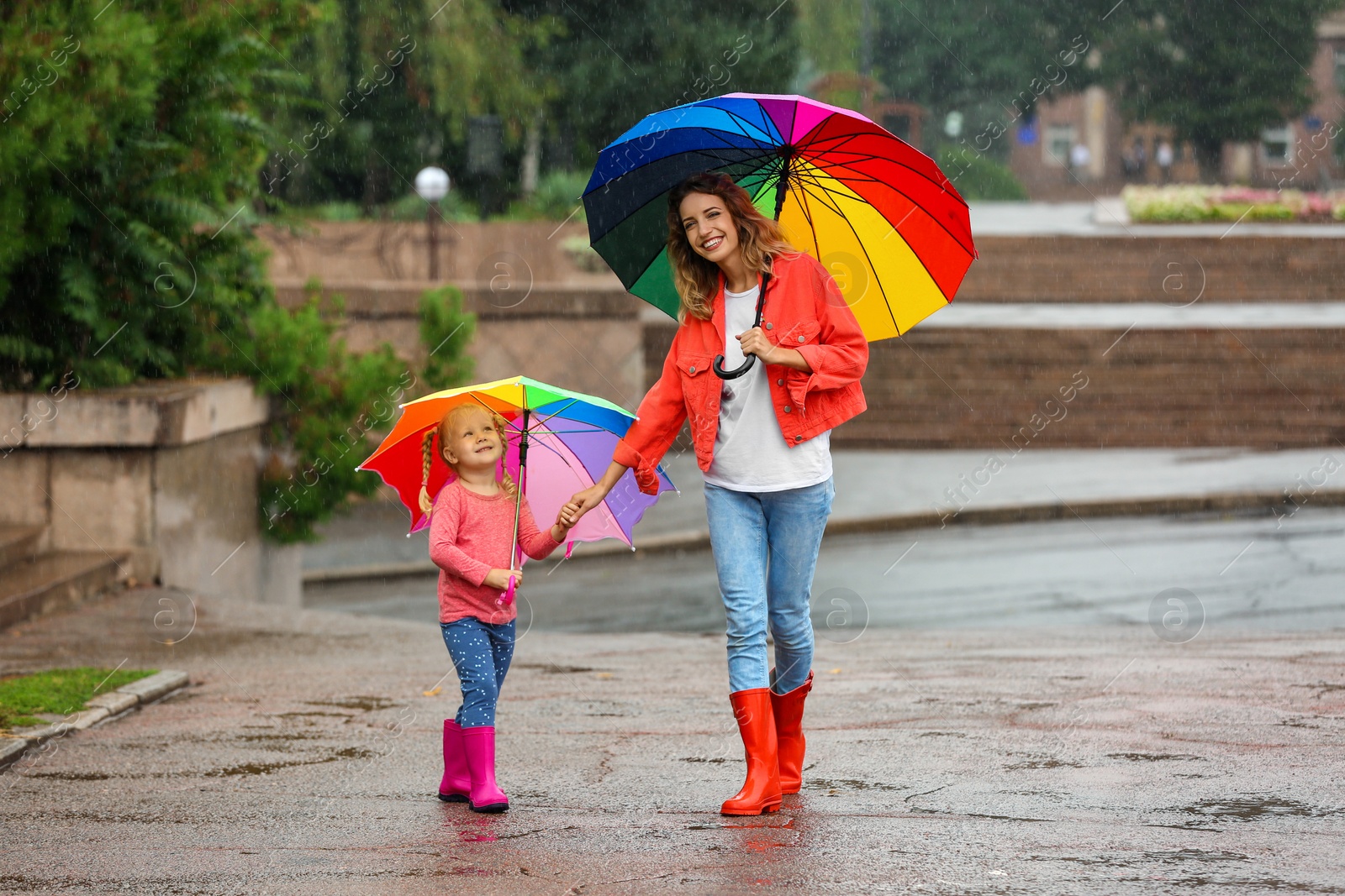 Photo of Happy mother and daughter with bright umbrella under rain outdoors