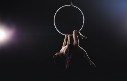 Photo of Young woman performing acrobatic element on aerial ring indoors
