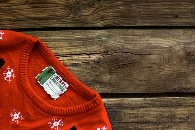 Photo of Christmas sweater with tag on wooden background, top view. Space for text