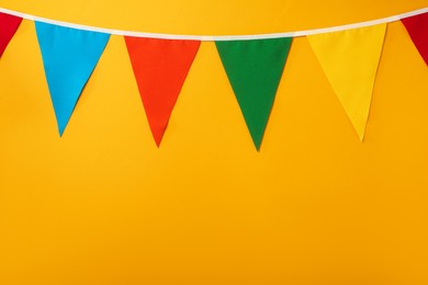 Photo of Bunting with colorful triangular flags on orange background. Space for text