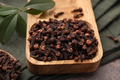 Photo of Wooden tray with aromatic cloves and green leaves on table, closeup