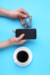 Online payment. Man with smartphone, credit card and coffee on light blue background, top view