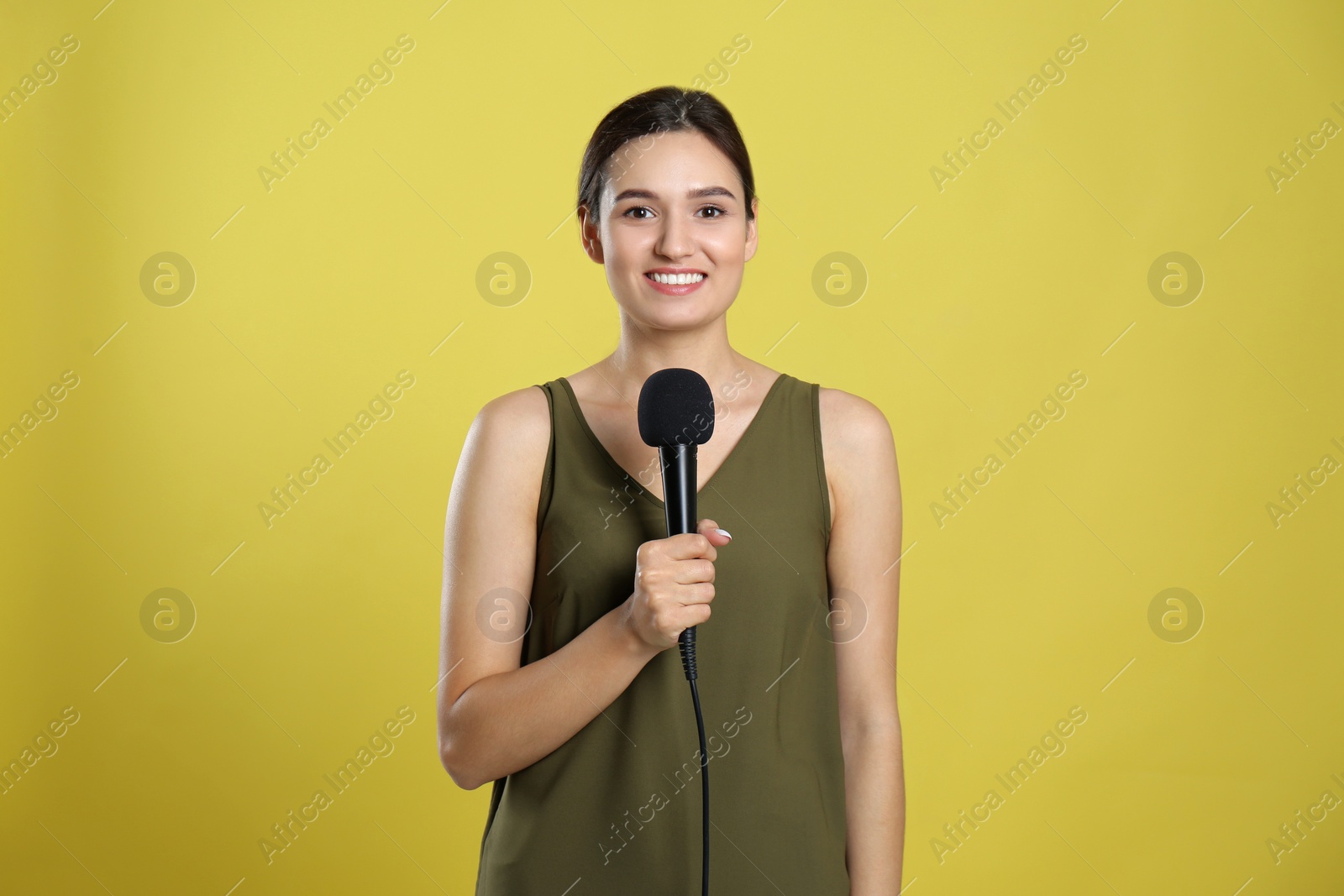 Photo of Young female journalist with microphone on yellow background