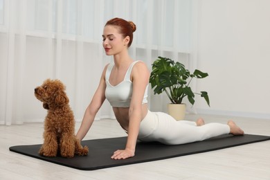 Photo of Young woman practicing yoga on mat with her cute dog indoors