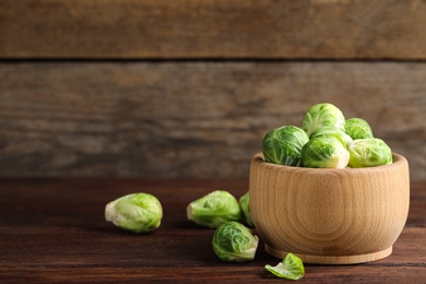 Bowl with fresh Brussels sprouts on brown wooden table, closeup. Space for text