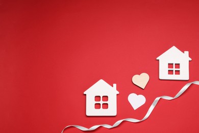 Photo of White ribbon and decorative hearts between two house models symbolizing connection in long-distance relationship on red background, flat lay with space for text