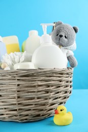Photo of Wicker basket with different baby cosmetic products, bathing accessories and toys on light blue background