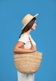 Young woman with stylish straw bag on light blue background