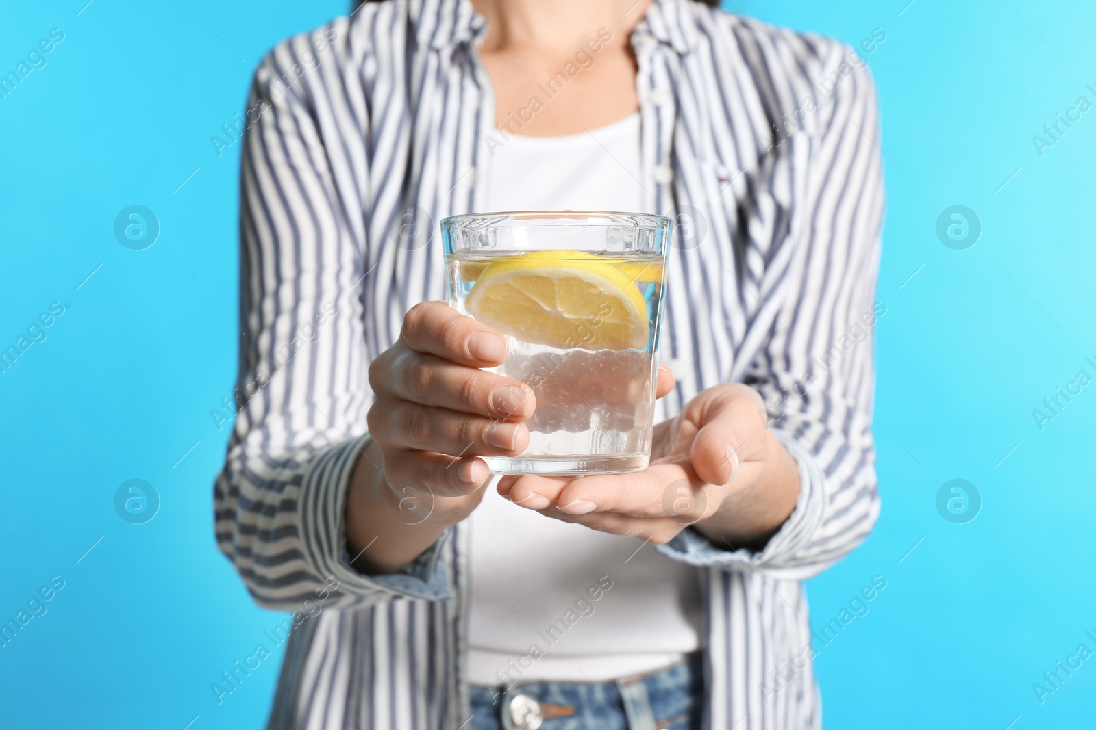 Photo of Young woman with glass of lemon water on light blue background, closeup