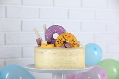 Delicious cake decorated with sweets and balloons against white brick wall