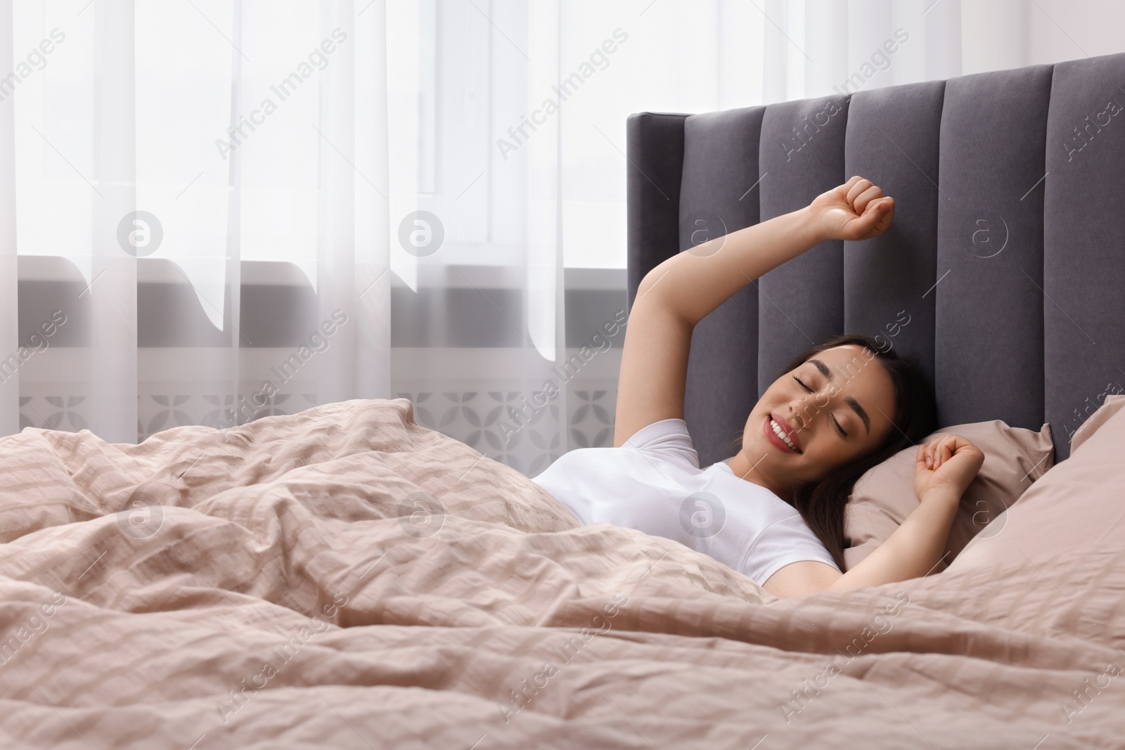 Photo of Beautiful woman stretching in soft bed at home, space for text. Lazy morning