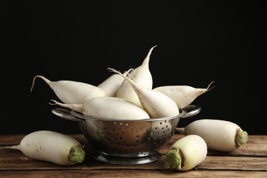 Photo of Colander with white turnips on wooden table