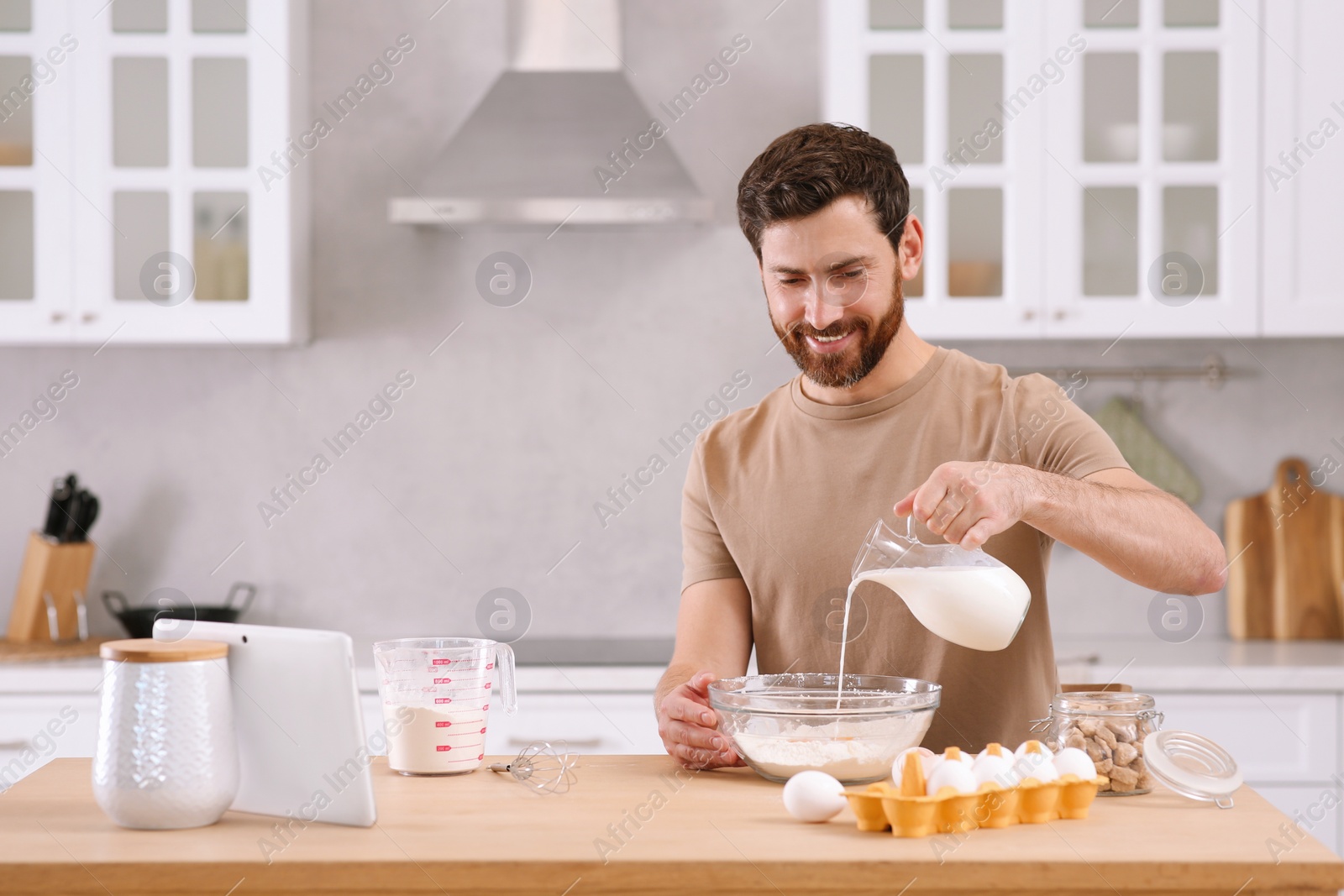 Photo of Man making dough while watching online cooking course via tablet in kitchen