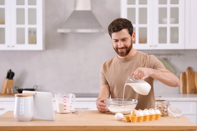 Man making dough while watching online cooking course via tablet in kitchen