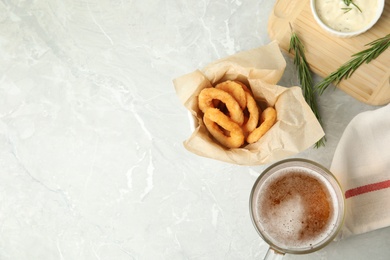 Delicious crunchy fried onion rings and glass of beer on grey marble table, flat lay. Space for text