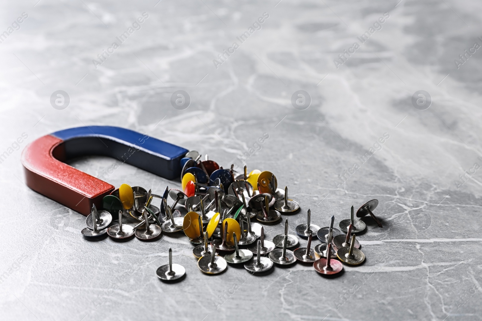 Photo of Red and blue horseshoe magnet attracting push pins on grey marble background